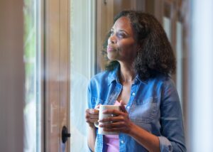 a person holding a cup of coffee looking outside their window reflecting about life.