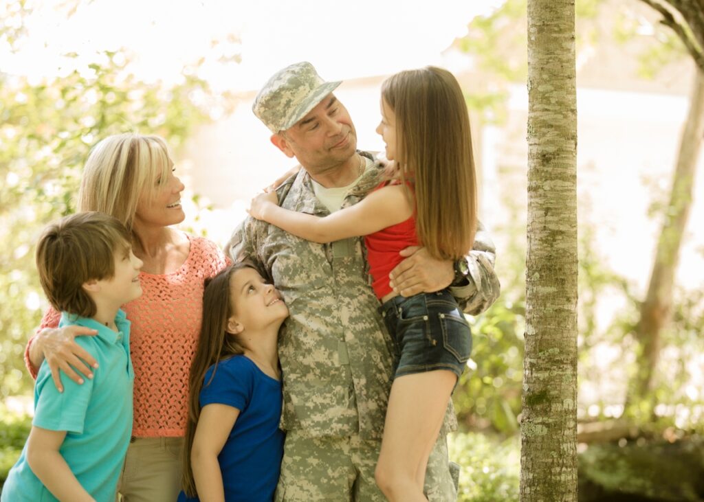 a veteran with his family holding his kid and his two other kids hugging him and his wife