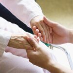 a picture of a caretaker holding an elderly womans hands while she sits in her wheelchair.