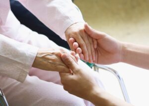 a picture of a caretaker holding an elderly womans hands while she sits in her wheelchair.